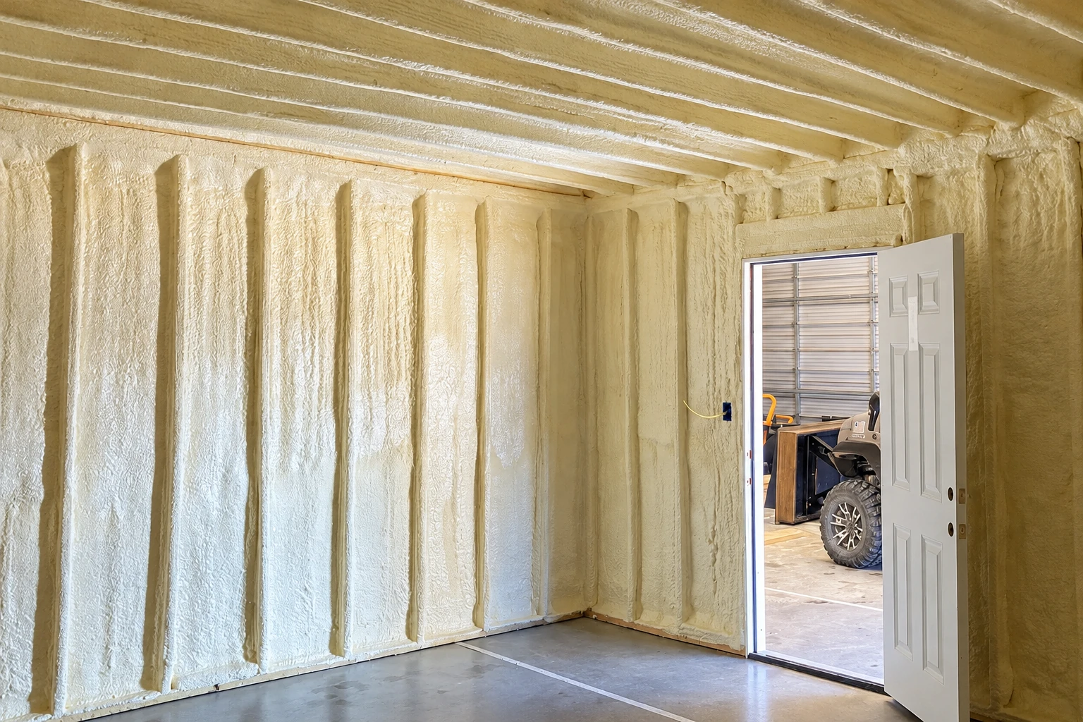 Commercial space with cream-colored spray foam covering the walls and ceiling around exposed framing.
